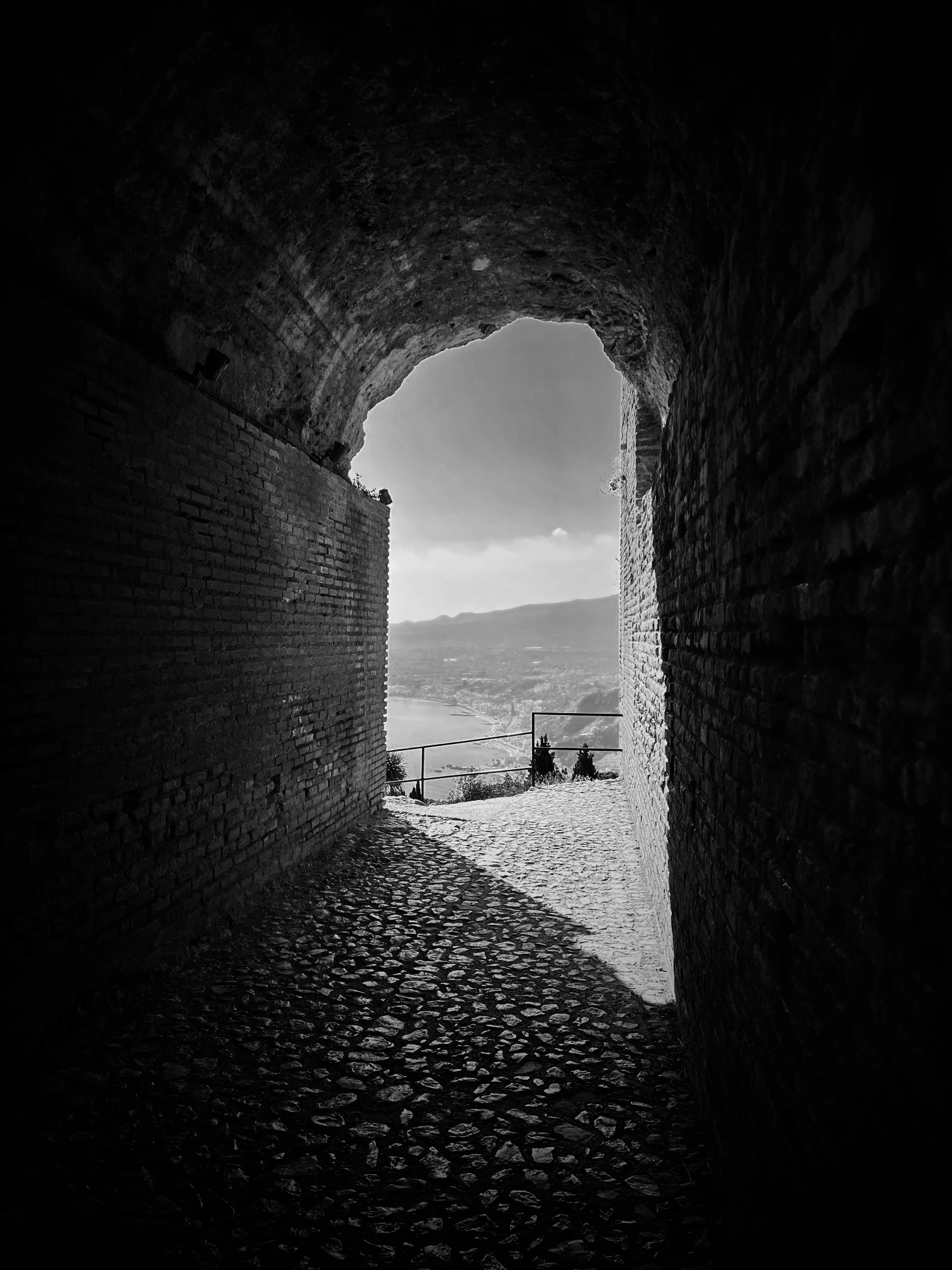 A black-and-white view through a stone passage toward the coast